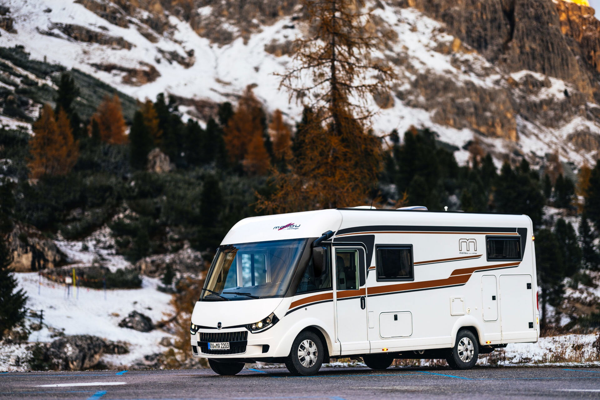 Malibu Reisemobil von der Seite, außen vor einem großen Berg mit teilweise Schnee.