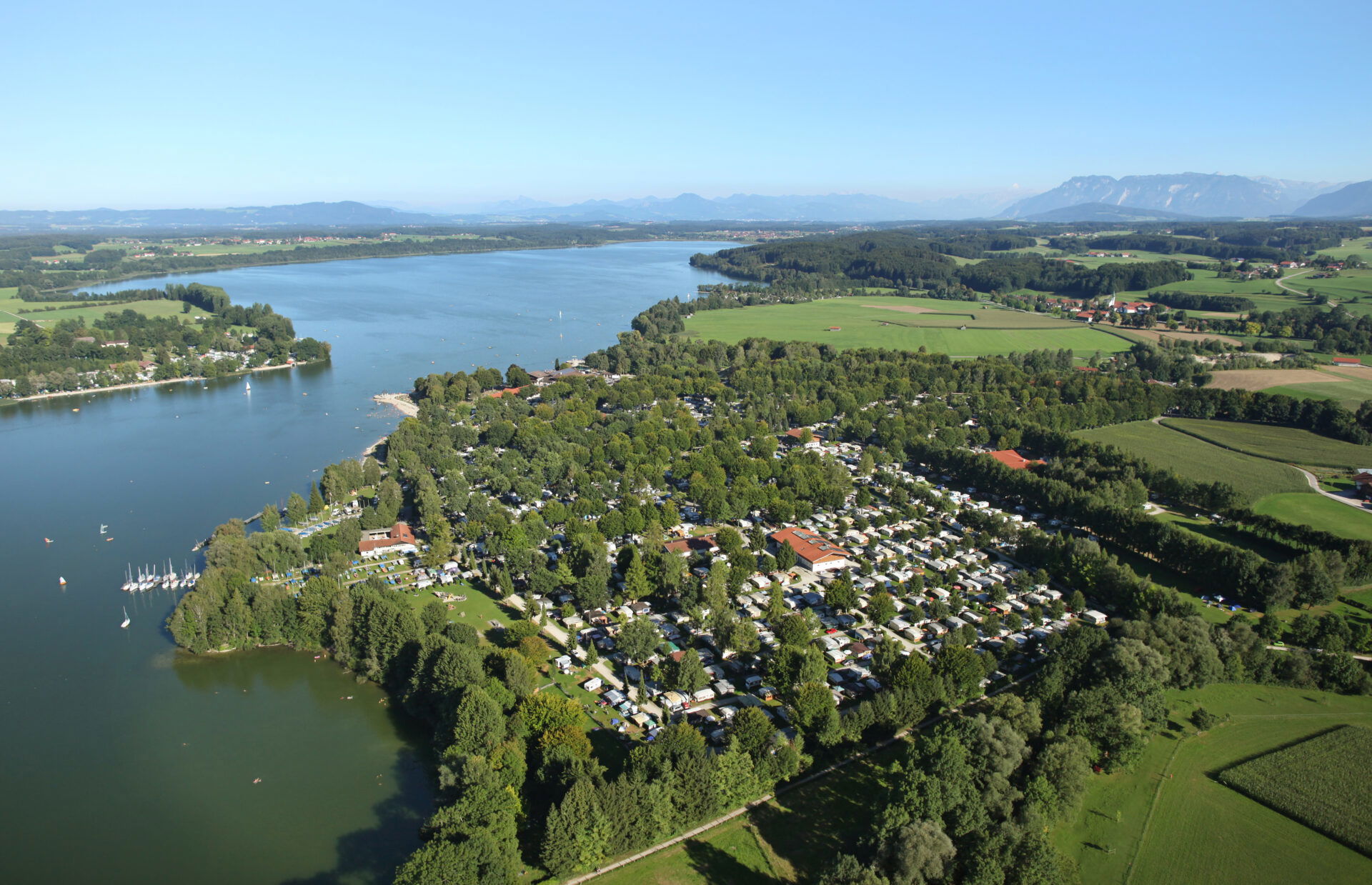 Campingplatz mit vielen Wohnmobilen inmitten der Natur und viel Grün. Links davon ist der Waginger See.