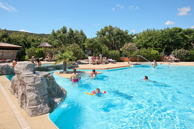 Schwimmbecken mit vielen Kindern und Erwachsenen in der Sonne.