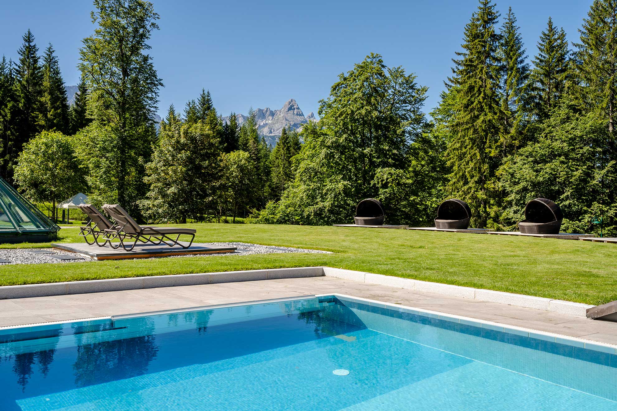 Pool umgeben von einer grünen Wiese und Nadelbäumen