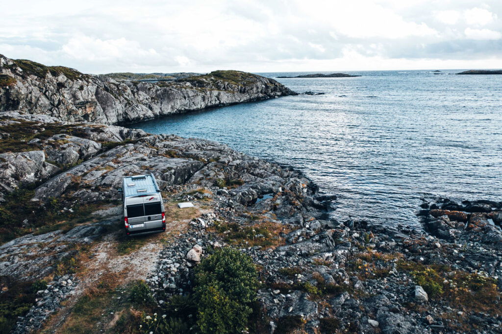 Malibu Wohnmobil geparkt an einer Küstenstraße in Italien, umgeben von einer malerischen Landschaft mit Meerblick und felsigen Klippen im Hintergrund.